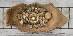 large broken earth ware dish with rocks and egg inside a nest.