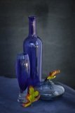 Blue Glass and Bottles with two orange leaves against a blue grey background..